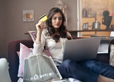 A girl sitting on the couch with a laptop and a credit card in her hand